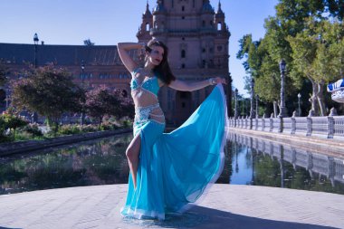 Orta yaşlı, turkuaz elbiseli, yapay elmaslı İspanyol kadın göbek dansı figürleri yapıyor. Göbek dansı konsepti.