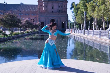 Orta yaşlı, turkuaz elbiseli, yapay elmaslı İspanyol kadın göbek dansı figürleri yapıyor. Göbek dansı konsepti.