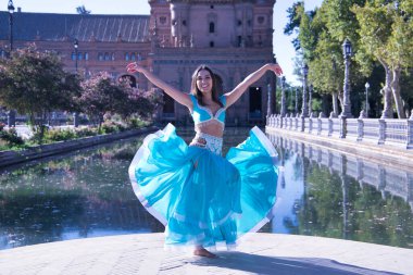 Orta yaşlı, turkuaz elmaslı İspanyol kadın, göbek dansı yaparken elbisesini kaldırıyor. Göbek dansı konsepti.