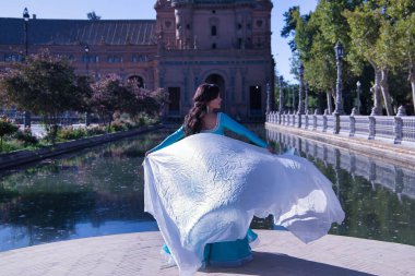 Orta yaşlı, turkuaz elbiseli, yapay elmaslı İspanyol kadın, beyaz peçeli göbek dansı. Göbek dansı konsepti.