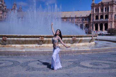 Orta yaşlı İspanyol kadın, suni elmaslı güzel bir elbise giyiyor, göbek dansı için, etrafında sabun köpükleriyle çeşmenin önünde dans ediyor. Göbek dansı konsepti.