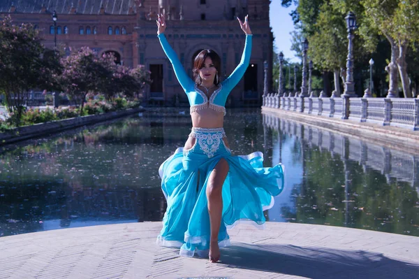 Orta yaşlı, turkuaz elmaslı İspanyol kadın, göbek dansı yaparken elbisesini kaldırıyor. Göbek dansı konsepti.