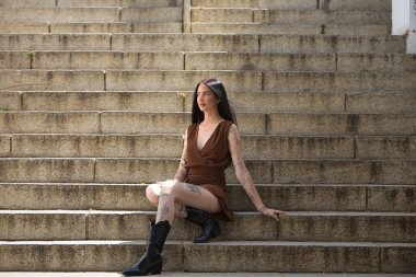 Genç bir kadın, esmer, uzun boylu, zayıf ve çok dövmeli, kahverengi elbiseli ve çizmeli, sonsuzluğa bakıyor, tatlı, masum ve yalnız, merdivenlerde oturuyor. Gençlik kavramı, asilik, milenyum..