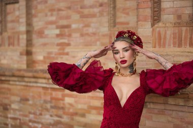 Genç, güzel, sarışın, kırmızı flamenko elbiseli, saçında çiçekler ve altın mücevherlerle İspanya meydanında flamenko dansı yapan bir kadın. Dans konsepti, sanat, tipik İspanyol..