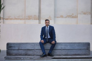 Genç, esmer, İspanyol, modern yönetici, takım elbiseli ve kravatlı, ekonomik kriz konusunda ciddi ve endişeli, mola alıyor, kentteki ahşap bir bankta oturuyor. Konsept iş, şirket, lider.