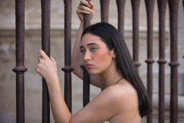 Genç, güzel, koyu saçlı, mavi gözlü, üzgün ve endişeli bakışları olan bir İspanyol kadının portresi, bir çite yapışmış, kadınlara yapılan baskıyı temsil ediyor. Konsept: model, güzellik, moda, eğilim.