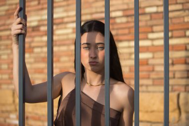 Genç bir kadın, güzel, esmer, mavi gözlü, İspanyol, zarif kahverengi bir şifon elbise giyiyor, ciddi ve hüzünlü bir ifadeyle, parmaklıklar arkasında tutuluyor, kadınların zulmünü temsil ediyor..