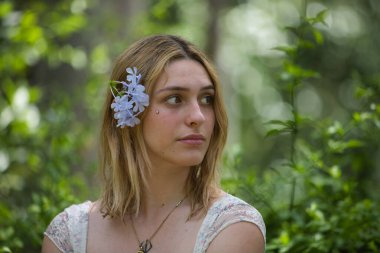 Genç, güzel, sarışın bir kadının portresi, çiçekli bir elbise giyiyor, uzaktan bakıyor, saçında bir buket menekşe ile, açık hava parkında. Güzellik kavramı, gençlik, milenyum.