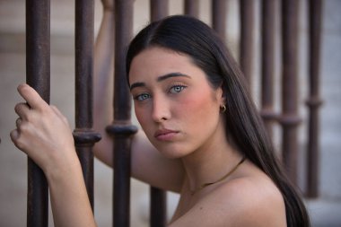 Genç, güzel, koyu saçlı, mavi gözlü, üzgün ve endişeli bakışları olan bir İspanyol kadının portresi, bir çite yapışmış, kadınlara yapılan baskıyı temsil ediyor. Konsept: model, güzellik, moda, eğilim.