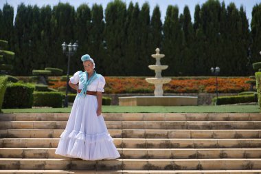 Genç, güzel, sarışın kadın tipik Endülüs flamenko kostümlü açık mavi şallı ve çiçekli hac için merdivenlerde poz veriyor. Konsept bölgesel kostümler, tipik, İspanyolca.