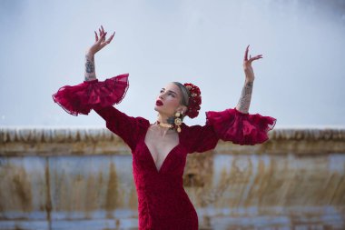 Genç, güzel, sarışın, kırmızı flamenko elbiseli, saçında çiçekler, altın mücevherler, Seville 'de İspanya meydanında fıskiyeli fıskiyelerle flamenko pozları veriyor..