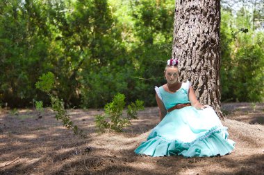 Genç bir kadın, güzel, sarışın, tipik Endülüs flamenko kostümlü açık mavi renkli, bir ağacın gölgesinde dinlenen. Konsept bölgesel kostümler, tipik, İspanyolca