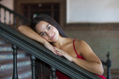 Genç, esmer, kırmızı elbise giyen Latin bir kadının portresi. Tatlı ve narin. Kameraya bakıyor, korkuluklara yaslanıyor. Kavram: gençlik, bakışlar, şefkat, masumiyet.