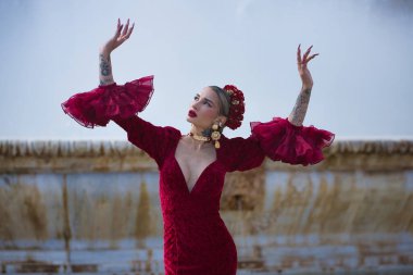 Genç, güzel, sarışın, kırmızı flamenko elbiseli, saçında çiçekler, altın mücevherler, Seville 'de İspanya meydanında fıskiyeli fıskiyelerle flamenko pozları veriyor..