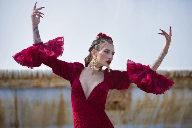 Genç, güzel, sarışın, kırmızı flamenko elbiseli, saçında çiçekler, altın mücevherler, Seville 'de İspanya meydanında fıskiyeli fıskiyelerle flamenko pozları veriyor..