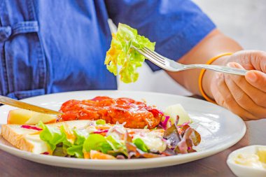 Kadınlar salatadan sebze toplamak için çatallaşıyor. Kızarmış domuz bifteği ve beyaz tabak.