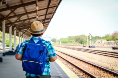 Asyalı küçük bir çocuk mavi bir sırt çantası taşıyor. Trenin okula gitmesini bekliyor.
