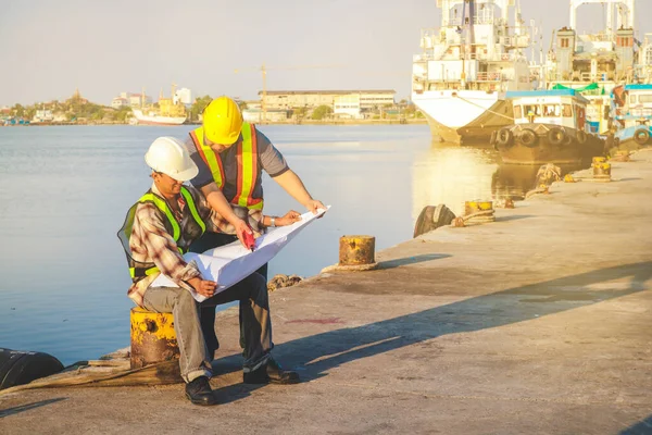 Two harbor engineers watch the paper, construction work, discuss the work to achieve the goal.