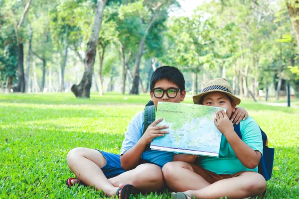 一个小学的亚洲男孩坐在花园里的草坪上 手里拿着一张地图来研究这个信息 — 图库照片