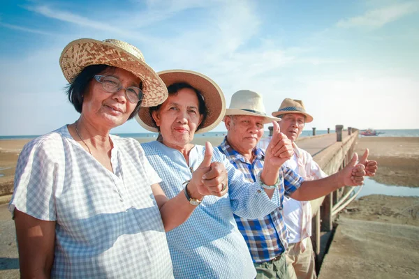 A group of elderly friends meet to relax at the sea. They are healthy and happy. Thumbs up