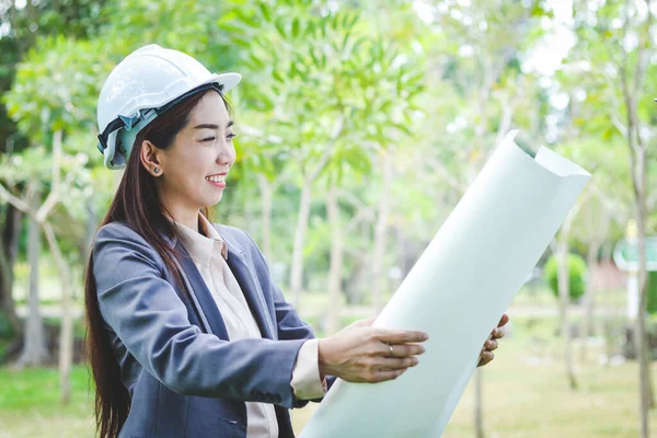 Female engineers wear white safety helmets, hold paper for building construction.