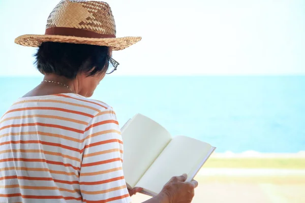 一位年长的亚洲女人在海边看书 — 图库照片