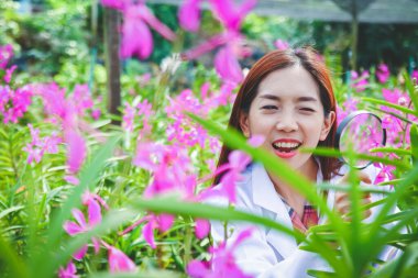 Güzel araştırmacılar çiçekleri görmek ve araştırmaya bilgi getirmek için bir büyüteç tutuyorlar..