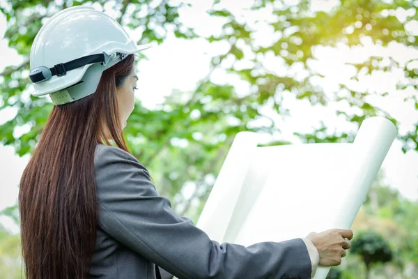 Female environmental engineer wearing a suit, wearing a white hat, standing holding a paper plan