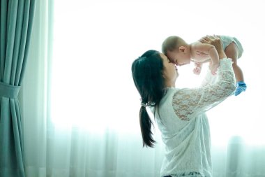 Genç bir anne yeni doğmuş bir bebeği kollarında tutuyor. İkisi de yatak odasındaydı, pencerenin yanında duruyorlardı..