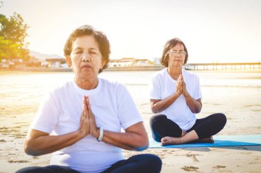 Deniz kenarında egzersiz yapan, yoga yapan iki Asyalı yaşlı kadın..