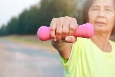 Yaşlı kadın el kaldırma 1 kg dambıl pembe, egzersiz Gökyüzü arka planı