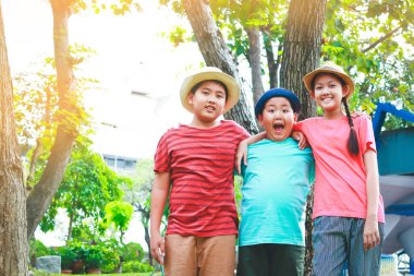 Üç Asyalı çocuk ayakta, birbirlerine sarılıyorlar, geziye gitmekten memnunlar.