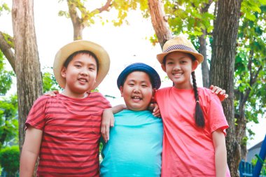 Üç Asyalı çocuk ayakta, birbirlerine sarılıyorlar, geziye gitmekten memnunlar.