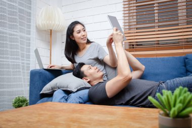 Asyalı genç çift tatillerde evlerindeki mavi kanepelerinde oturup rahatlarlar. Aile kavramı, evde çalışmak. Boşluğu kopyala