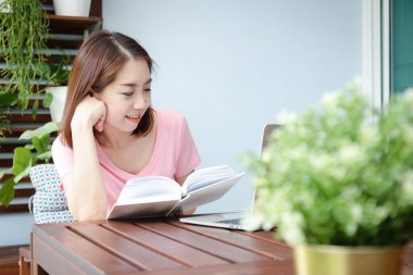 Kitap okuyan Asyalı kadın arkana yaslan ve balkonda rahatla. Sağlık hizmeti kavramı