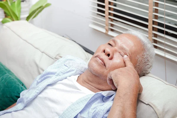 An elderly Asian man has eye pain. Sit on the sofa in the lounge. Senior health care concept