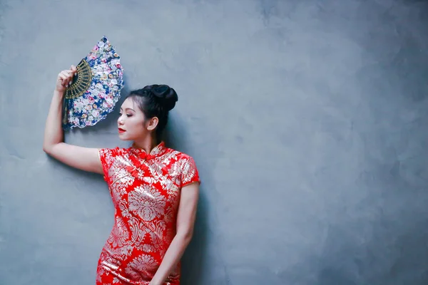 Young woman wearing red Chinese dress Welcome the new year Holding a blue fan The background is a plaster wall. Have space to write messages