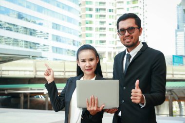 Kadınlar ve erkekler takım elbise giyip bilgisayar tutuyorlar. Konuşuyorlar, iş yapıyorlar.