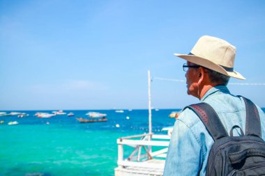 Sahilde şapka takan yaşlı bir Asyalı.