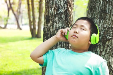 Yeşil kulaklık takan çocuklar ağaca yaslanmış, gözleri kapalı, mutlular. Eğitim kavramı. Boşluğu kopyala