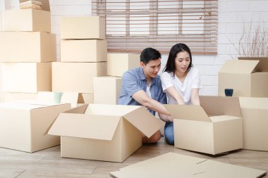 Yeni bir eve taşınan Asyalı çift evi dekore etmek için kahverengi karton kutuyu boşaltmaya yardım ediyor. Yeni bir hayata başlama, aile kurma kavramı. Boşluğu kopyala