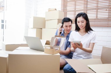 İnternette iş yapan Asyalı çift ürünü postayla gönderiyor. Evde çalışırken bilgisayar ve akıllı telefonlar kullanarak video konferanslarıyla bir şeyler sat..