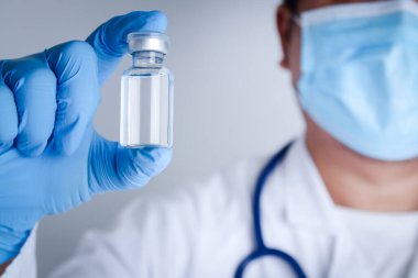 Doktor ya da araştırmacı mavi eldiven giyip laboratuvarda çalışıyor. Coronavirus veya COVID-19 'u tedavi etmek için sıvı bir aşı şişesi al. Hastane sağlık hizmetleri
