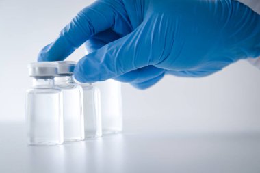 Doktor ya da araştırmacı mavi eldiven giyip laboratuvarda çalışıyor. Coronavirus veya COVID-19 'u tedavi etmek için sıvı bir aşı şişesi al. Kavramsal hastane tıbbi hizmetleri