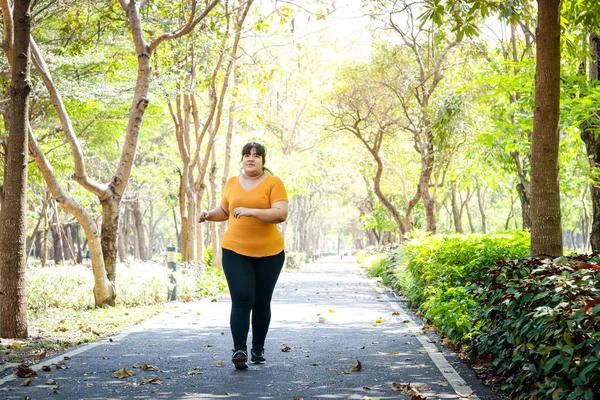 Fat Asian woman wearing yellow blouse Jogging in the morning In the park. Concept of weight loss Exercise for the good health of obese people. Copy space
