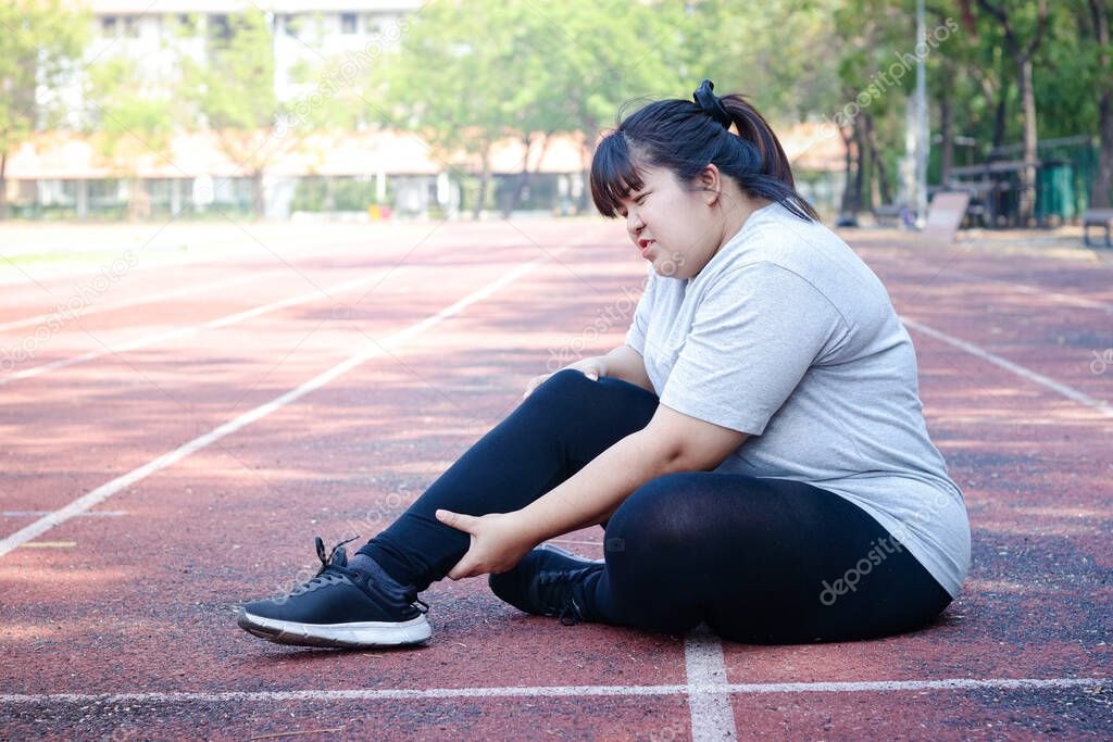 Fat Asian woman injured from jogging Sitting on the floor, holding the right ankle, felt a lot of pain. Concepts of weight loss, exercise, health problems