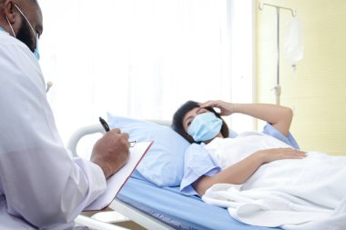 Afro-Amerikalı erkek doktor hastane yatağında yatan bir kadının hastalığını kontrol et. Koronavirüs salgını sırasında hastaların tedavisi. Tıbbi hizmet kavramı.