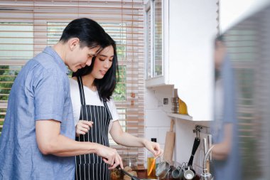 Asyalı çiftler evdeki mutfakta birlikte yemek pişirirler. Onlar mutlu. Aile kavramı, yemek pişirme, COVID-19 sırasındaki geçim kaynakları, sosyal mesafeler. Boşluğu kopyala