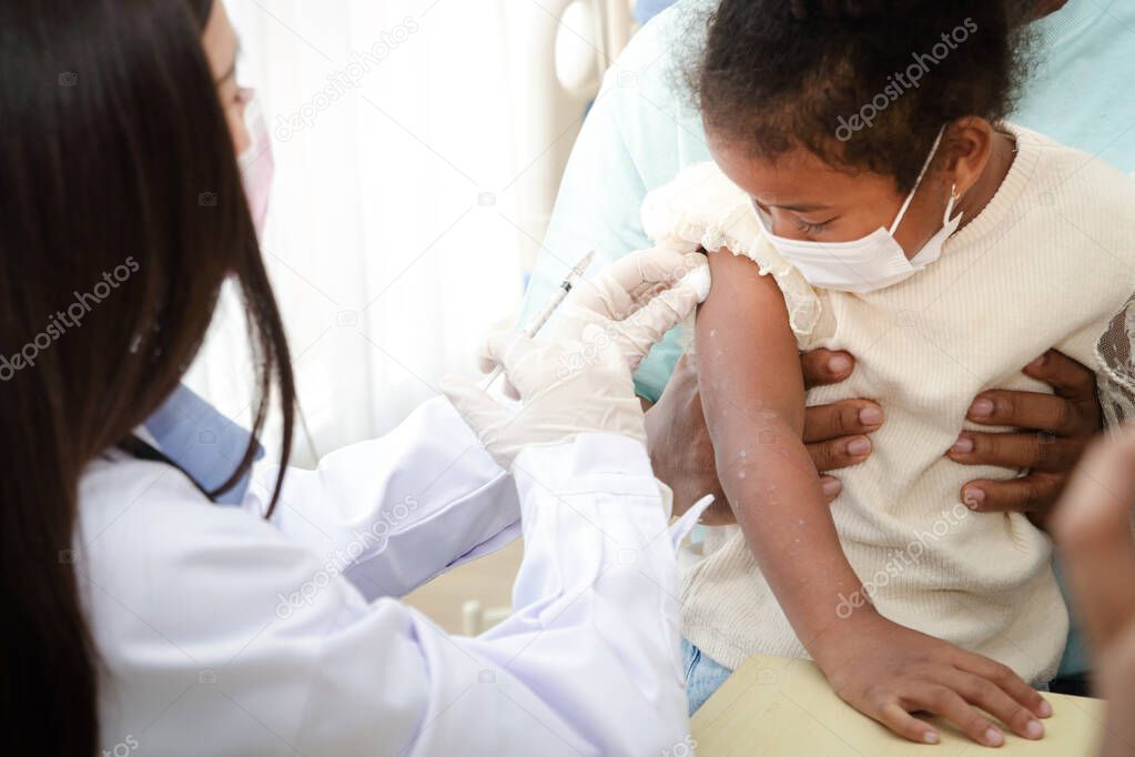 Doctors inject a vaccine in the arm of a young African-American girl to strengthen immunity and protect it from diseases. Concept of the vaccine against COVID-19. Medical services in hospitals.