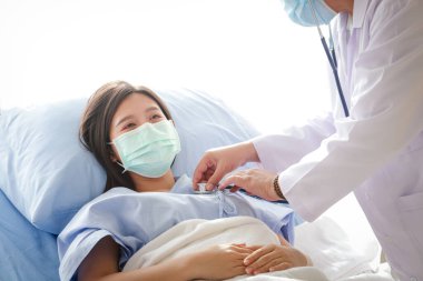 Doktor maske takan genç bir kadının sağlığını kontrol etmek için steteskop kullandı ve hastane yatağında yattı. Coronavirüs salgını sırasında hastaların tedavisi. Tıbbi servis kavramı kopyalama alanı